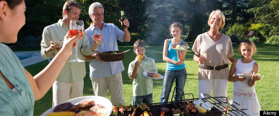 AHYDYR Three generation family standing beside barbecue grill in garden adults raising wine glasses in toast smiling